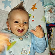 Malone participe au concours pour gagner de l'argent avec cette photo : apparel, baby, bib, blue_eyes, changing_mat, child, clothing, colorful, cute, diaper, face, hand, happy, indoor, infant, joyful, mohawk, pattern, playful, smiling