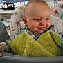 baby, high_chair, smiling, bib, face, child, indoor, couch, television, living_room, furniture, person, clothing, colorful, star_pattern, happy, seat, cute, young_child, home