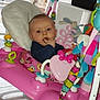 baby, child, indoor, toy, pink, activity_chair, stuffed_animal, colorful, fingers_in_mouth, curious, blue_clothing, floor_tiles, window, cushion, play_area, face, person, seat, infant, soft_toy