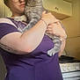 Loki joined the competition — help win amazing prizes! person, cat, glasses, purple_shirt, gray_tabby, blue_eyes, holding, kitchen, stove, cabinet, tattoo, bracelet, indoor, home, curious, smiling, short_hair, female, appliance, cozy