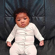 Tahyna participe au concours pour gagner de l'argent avec cette photo : baby, infant, onesie, white_clothing, black_leather, couch, furniture, indoor, child, person, face, curly_hair, sitting, expression, cute, young, portrait, comfortable, home, serious