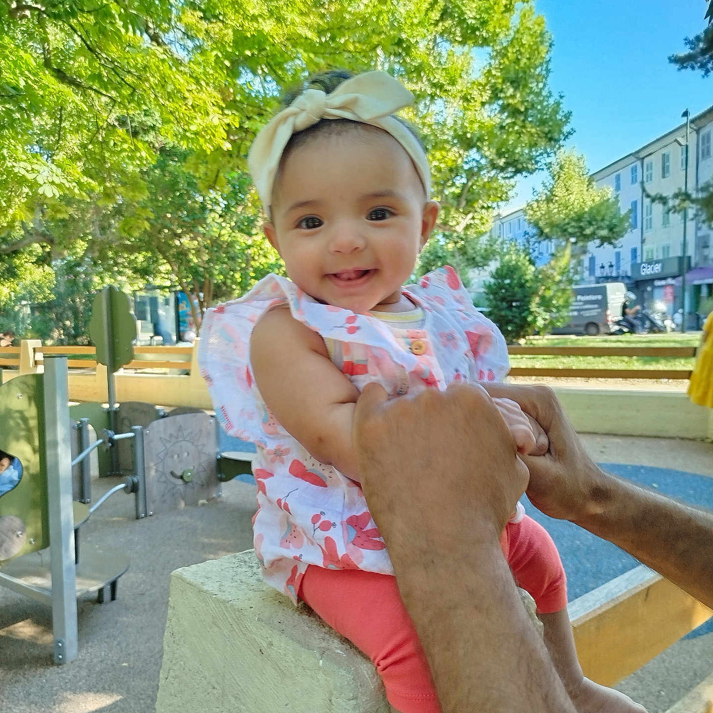 Oumayia joined the competition — help win amazing prizes! baby, bench, building, child, clothing, concrete, cute, daylight, fence, hands, happy, headband, infant, outdoor, park, person, playground, smiling, sunny, trees