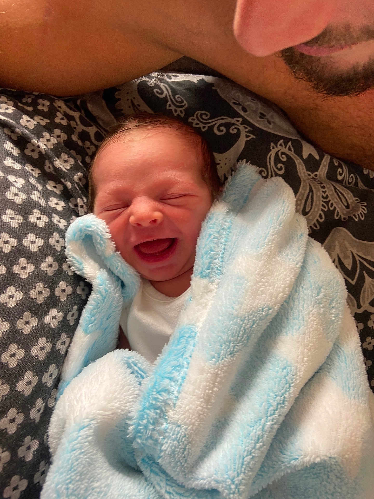 Rhys Junior is registered to the contest to win money with this photo: newborn, baby, smile, blanket, blue, white, pattern, fabric, person, adult, beard, closeup, happy, cozy, bed, wrapped, face, infant, portrait, love