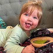 Bobbie joined the competition — help win amazing prizes! baby, child, smiling, tongue_out, happy, face, light_hair, blue_eyes, blanket, patterned_blanket, hand, bed, headboard, clothing, long_sleeve, indoor, portrait, cute, toddler, playful