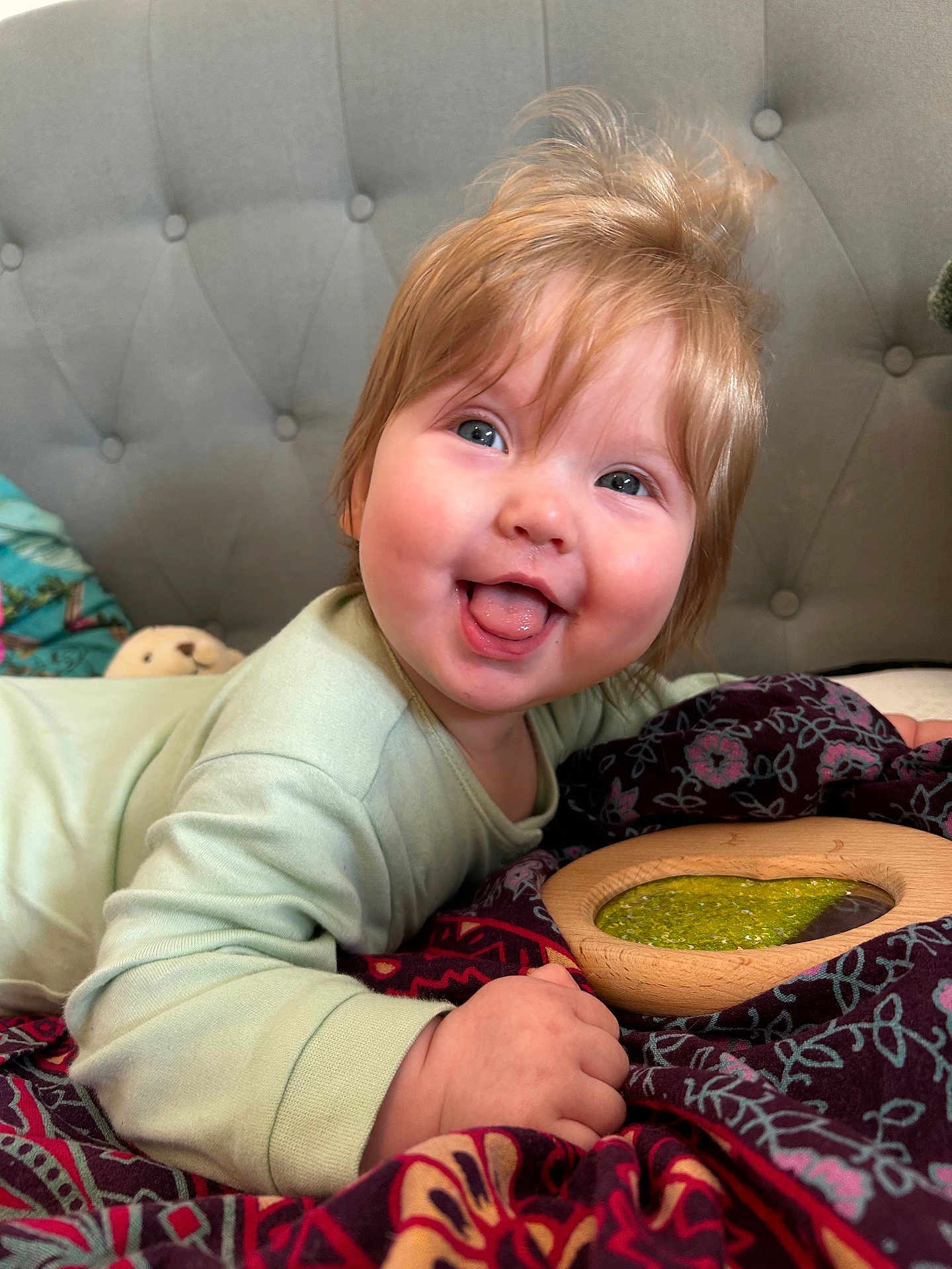Bobbie joined the competition — help win amazing prizes! baby, child, smiling, tongue_out, happy, face, light_hair, blue_eyes, blanket, patterned_blanket, hand, bed, headboard, clothing, long_sleeve, indoor, portrait, cute, toddler, playful