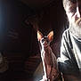 sphynx_cat, cat, person, beard, tattoo, deer_head_mount, indoor, couch, pillow, shadow, light_beam, wood_paneling, animal, pet, portrait, feline, sitting, face, ear, knee