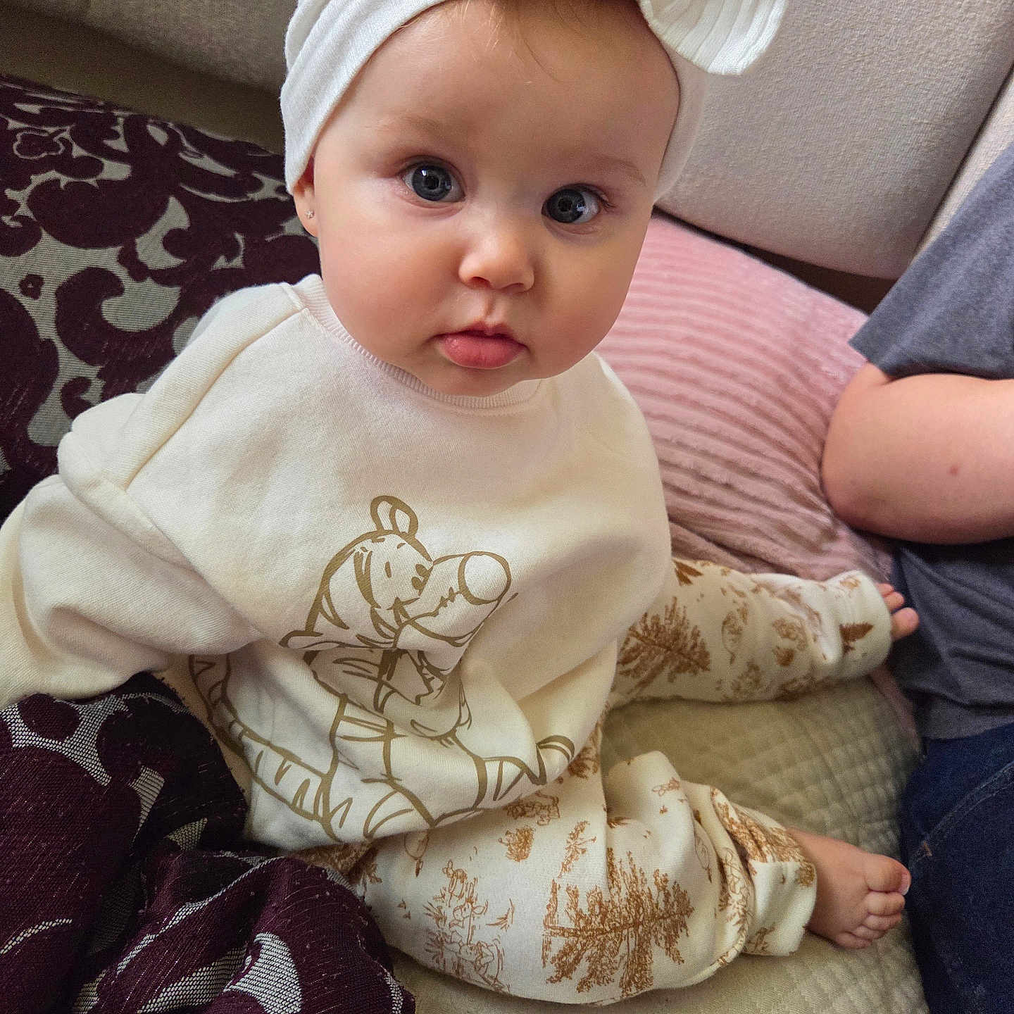 Alexandrya is registered to the contest to win money with this photo: baby, blanket, bow, cartoon_print, casual, child, curious, cushion, cute, face, foot, headband, home, indoor, infant, person, portrait, sitting, soft_lighting, white_clothing