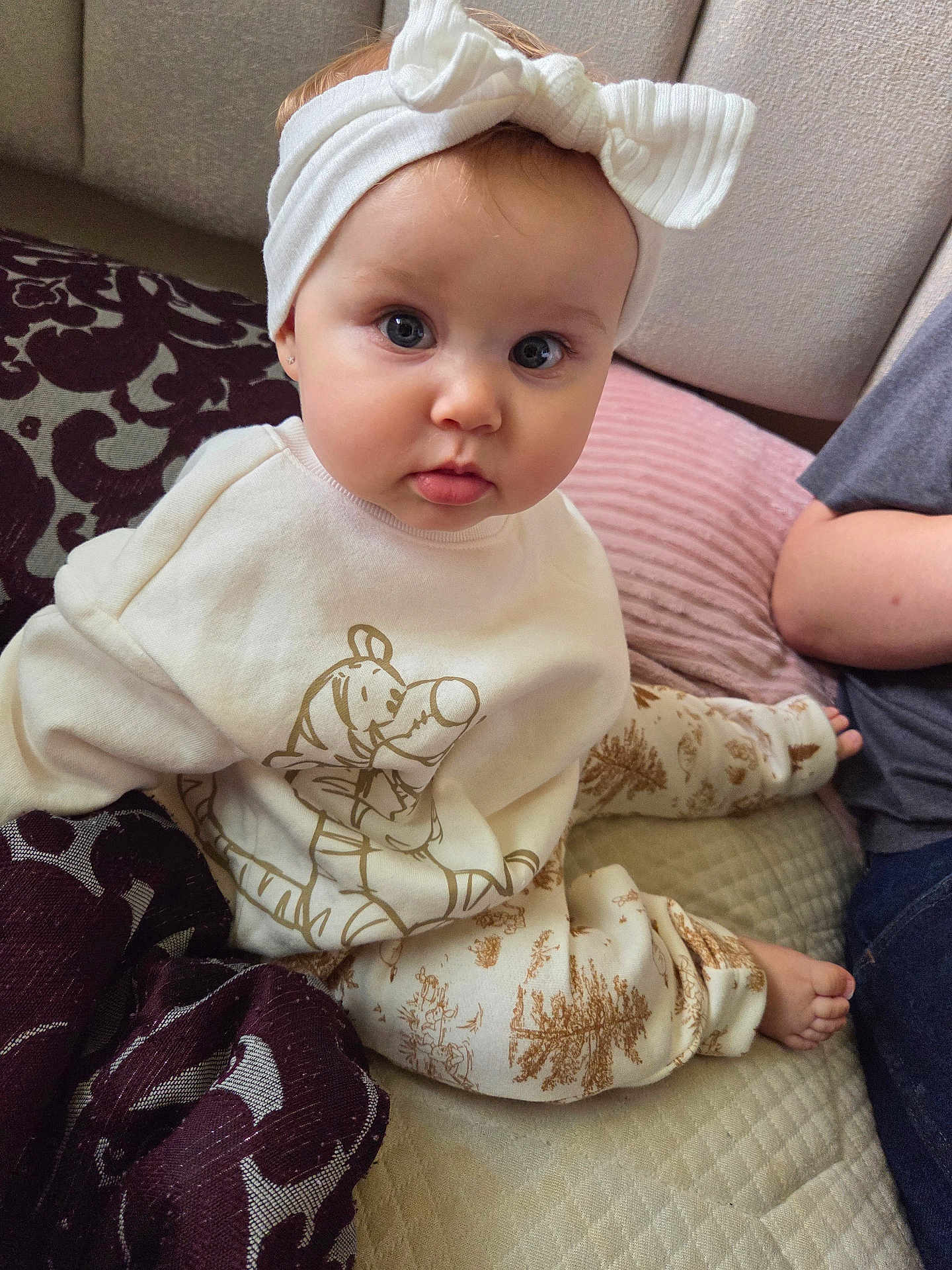 Alexandrya is registered to the contest to win money with this photo: baby, child, headband, bow, white_clothing, cartoon_print, sitting, cushion, blanket, indoor, curious, cute, portrait, face, foot, person, soft_lighting, casual, infant, home
