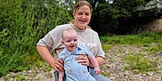Eli is registered to the contest to win money with this photo: child, baby, girl, outdoor, nature, rock, smile, happy, grass, trees, casual_clothing, jeans, onesie, footwear, headband, person, sitting, holding, infant, daytime