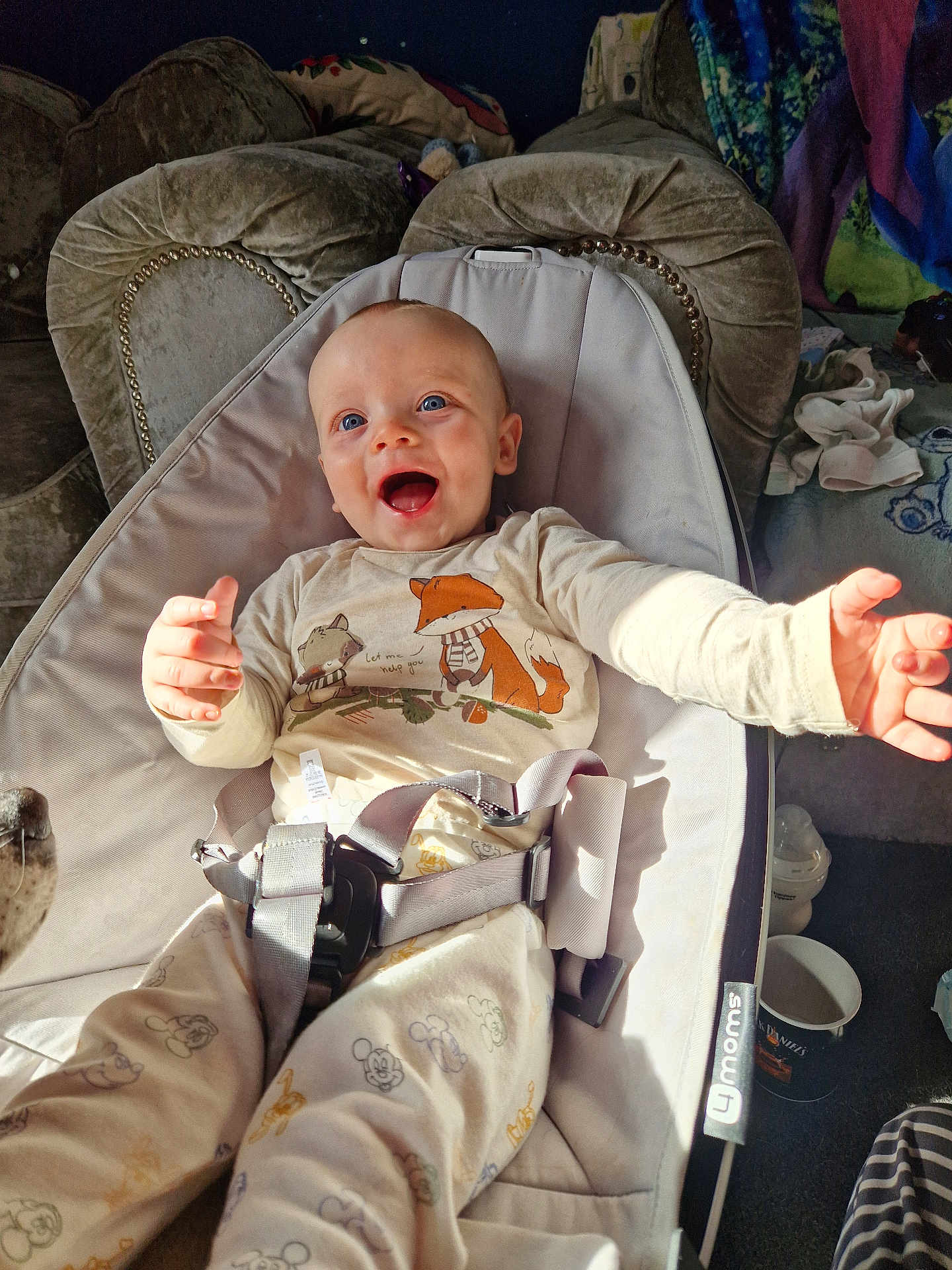 Eli is registered to the contest to win money with this photo: baby, smiling, blue_eyes, baby_rocker, pajamas, animal_prints, indoor, sunlight, happy, child, seat_belt, living_room, couch, blanket, clothing, person, infant, cute, reaching_out, comfort