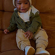 Teo joined the competition — help win amazing prizes! baby, child, couch, beanie, hat, smile, clothing, pants, jacket, shoes, indoor, person, seated, home, cardboard_box, cozy, cute, infant, relaxed, portrait