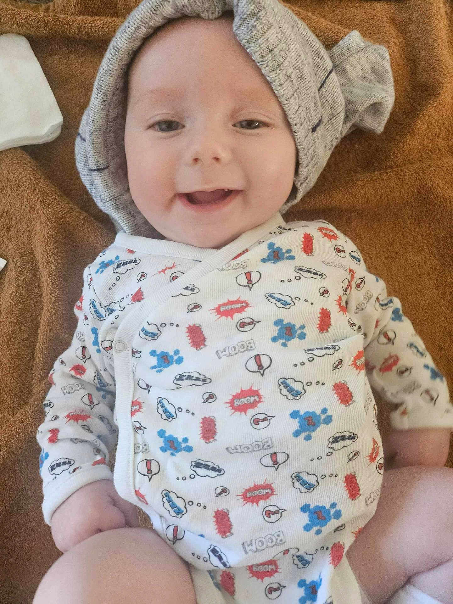 Roland participe au concours pour gagner de l'argent avec cette photo : baby, smiling, onesie, knitted_cap, blanket, happy, infant, cute, child, face, clothing, patterned, indoor, soft_texture, skin, laying_down, joy, expression, young_child, comfort