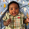 baby, child, smiling, plaid_shirt, buttoned_shirt, blanket, dinosaur_pattern, blue_blanket, curly_hair, indoor, portrait, happy, infant, cute, skin, face, hand, lying_down, cozy, clothing