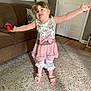 child, girl, smiling, dress, pink_bow, living_room, carpet, couch, sippy_cup, home_interior, wood_floor, door, lamp, pillow, happy, person, footwear, sandals, wall_clock, curtains