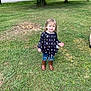 child, grass, outdoor, tree, boots, jeans, long_sleeve, skull_pattern, smiling, curly_hair, casual_clothing, daylight, nature, road, building, greenery, person, young_child, standing, playful