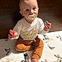 baby, child, pacifier, bed, duck_pattern, white_shirt, brown_pants, sitting, curious_eyes, indoors, soft_light, cute, infant, foot, hand, face, young_child, clothing, person, portrait