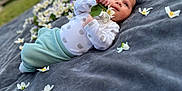 Thomas participe au concours pour gagner de l'argent avec cette photo : baby, infant, flower, blanket, outdoor, grass, nature, cute, portrait, child, young, soft, clothing, white, green, relaxing, lying_down, small, peaceful, daylight