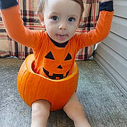 Matteo is registered to the contest to win money with this photo: toddler, child, pumpkin, orange_clothing, costume, halloween, outdoor, concrete, plaid_blanket, cute, baby, face, playful, smile, sitting, legs, hands, tongue, holiday, festive