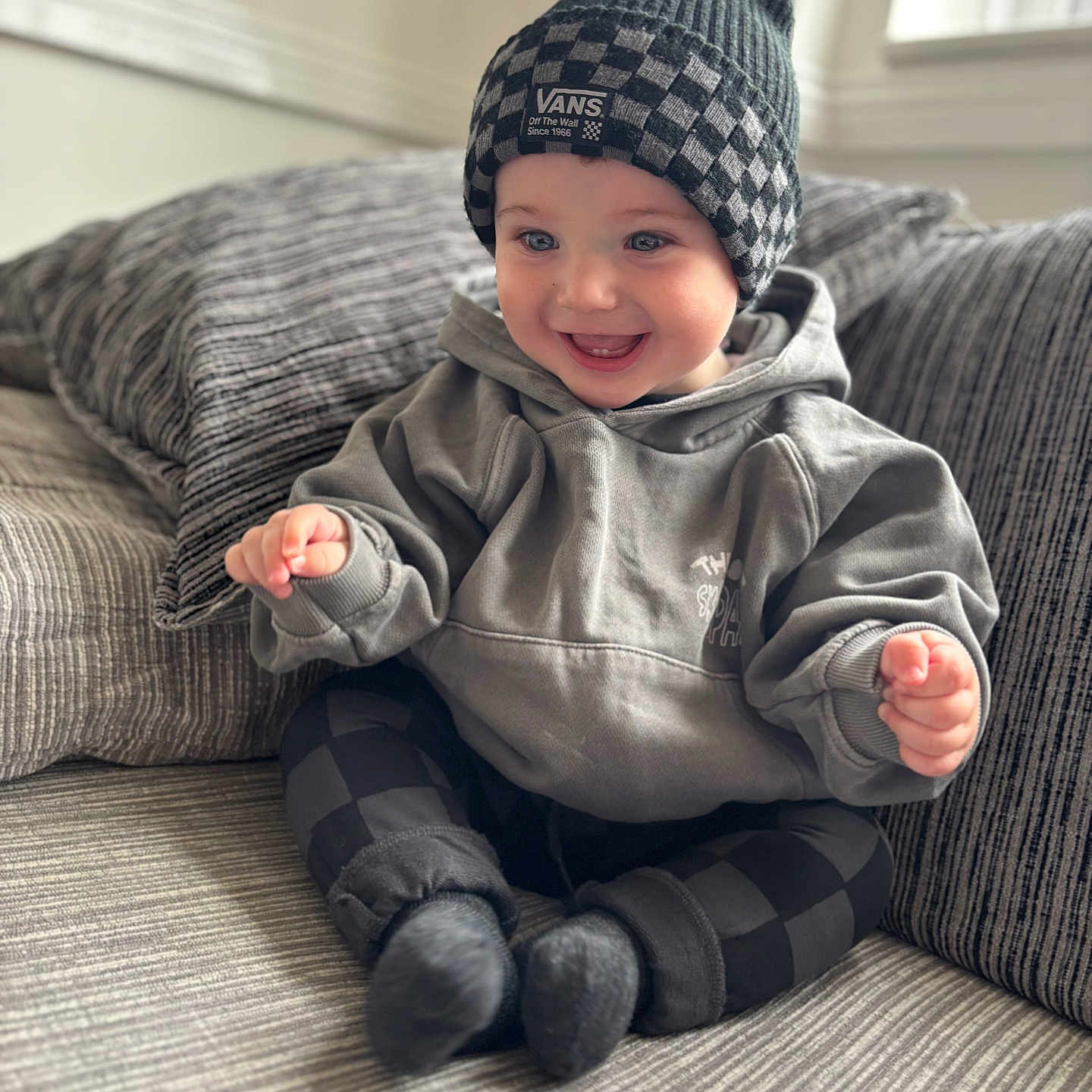 Luca joined the competition — help win amazing prizes! baby, beanie, casual, checkered_pattern, child, clothing, couch, cozy, cute, happy, home, hoodie, indoor, person, portrait, sitting, smile, sock, warm, young_child