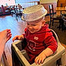 Christopher is registered to the contest to win money with this photo: toddler, child, high_chair, red_hoodie, aluminum_pie_tin, hat, smiling, restaurant, wooden_floor, chairs, tables, hand, white_shoes, indoor, playful, baby, person, casual_clothing, happy, seated