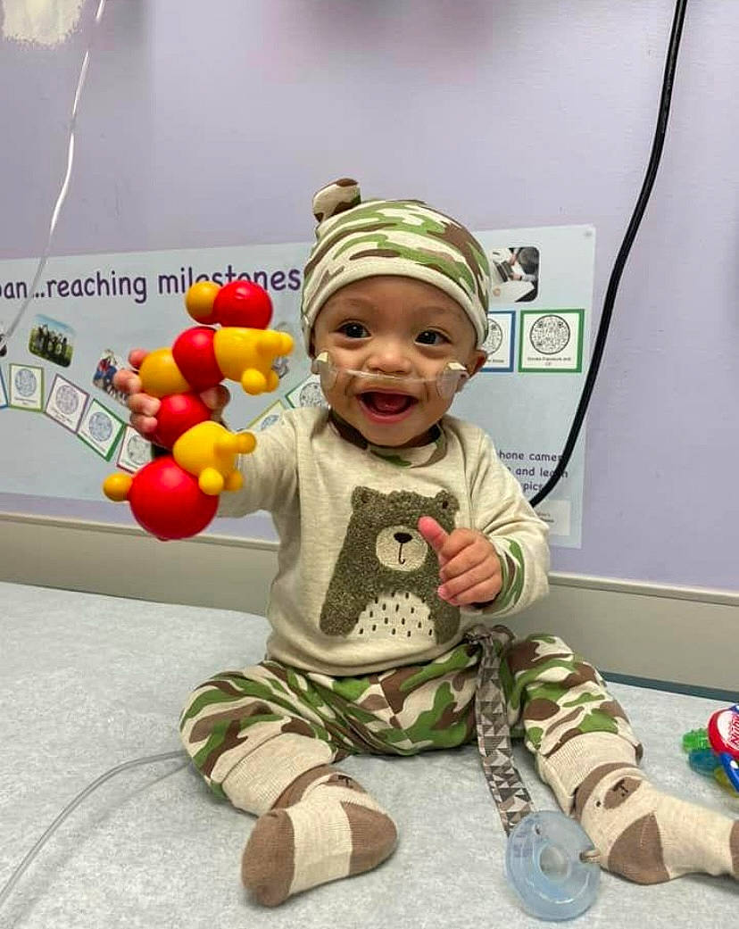 Judah joined the competition — help win amazing prizes! baby, baby_toddler_clothing, camouflage, cap, child, face, flooring, fun, happy, headwear, logo, military_camouflage, person, personal_protective_equipment, plant, play, recreation, room, sitting, sleeve