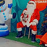 Pancho joined the competition — help win amazing prizes! person, dog, santa_claus, christmas, holiday, inflatable_snowman, costume, festive, beard, glasses, red_clothing, boots, decorations, tree, green_carpet, indoor, smiling, seated, pet, holding