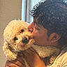 Pancho is registered to the contest to win money with this photo: person, dog, pet, fluffy, white_dog, curly_hair, indoor, window, affection, kiss, hug, close_up, love, cute, warm_light, human_hand, face, animal, friendship, cozy