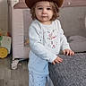 toddler, cowboy_hat, indoor, child, barefoot, pajamas, furniture, toy, baby_gates, curly_hair, floor, window, grey_cushion, wooden_floor, playpen, standing, cute, expression, home, person