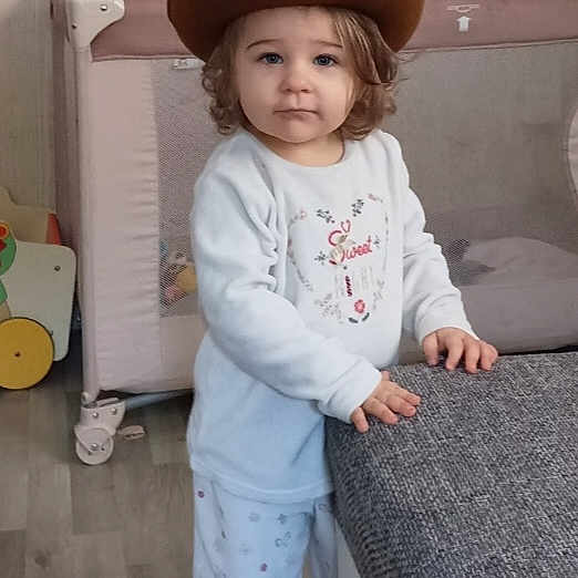 Abigaëlle a rejoint le concours — aidez-le/la à gagner de superbes lots ! toddler, cowboy_hat, indoor, child, barefoot, pajamas, furniture, toy, baby_gates, curly_hair, floor, window, grey_cushion, wooden_floor, playpen, standing, cute, expression, home, person