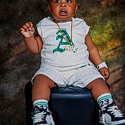 David is registered to the contest to win money with this photo: toddler, child, sitting, white_clothing, sneakers, gold_chain, watch, black_ottoman, curious_expression, studio_lighting, portrait, shorts, socks, fashion, cute, indoor, person, footwear, accessories, young_child