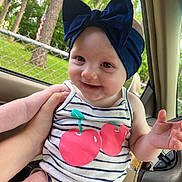 Meadow joined the competition — help win amazing prizes! baby, child, smiling, headband, bow, striped_clothing, cherry_print, hand, car_interior, window, trees, fence, greenery, happy, person, infant, cute, portrait, seat, casual