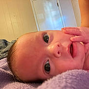 Athena is registered to the contest to win money with this photo: baby, closeup, hand, face, indoor, blanket, purple, skin, newborn, infant, person, young_child, resting, curious, eyes, expression, bed, door, human, child