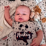 Kai is registered to the contest to win money with this photo: baby, infant, mickey_mouse, onesie, plush_toy, lion_toy, blanket, stars_pattern, child, cute, relaxed, lying_down, soft, cozy, indoor, portrait, smiling, hand, face, clothing