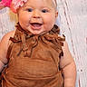 baby, background, blue_eyes, brown_outfit, child, closeup, cute, flower, fringe, happy, head_and_shoulders, headband, indoors, infant, one_person, pink_flower, portrait, sitting, skin, smiling