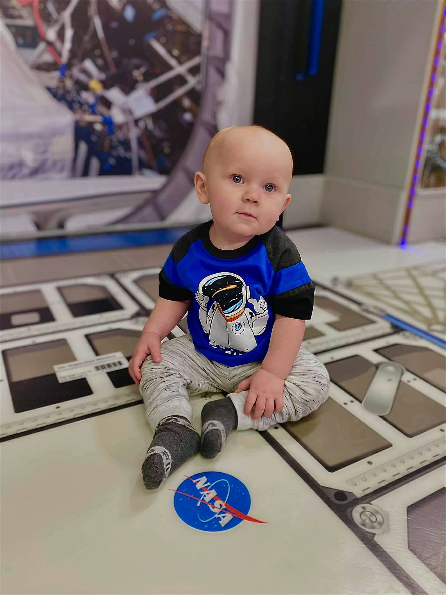 Graysen is registered to the contest to win money with this photo: baby, baby_toddler_clothing, blue, child, electric_blue, floor, flooring, font, fun, happy, hardwood, human_leg, machine, person, play, room, sitting, t_shirt, toddler, toy