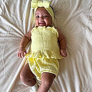 Kamila is registered to the contest to win money with this photo: baby, child, smiling, yellow_outfit, headband, lying_down, blanket, white_socks, cute, happy, infant, soft_texture, portrait, indoors, one_person, young_child, skin, clothing, baby_fashion, relaxed