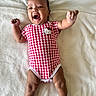 baby, infant, smiling, lying_down, onesie, red_and_white, checkered_pattern, hello_kitty, socks, soft_blanket, happy, cute, child, indoors, skin, person, portrait, small_ears, raised_arms, cheerful
