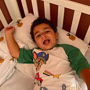 Jonas a rejoint le concours — aidez-le/la à gagner de superbes lots ! bed, bedding, bedroom, cartoon_shirt, child, crib, curly_hair, expression, green_sleeves, happy, indoor, person, pillow, playful, portrait, sleepwear, smiling, sunflower_pattern, white_bedding, young_child