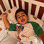 bed, bedding, bedroom, cartoon_shirt, child, crib, curly_hair, expression, green_sleeves, happy, indoor, person, pillow, playful, portrait, sleepwear, smiling, sunflower_pattern, white_bedding, young_child
