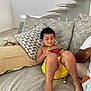 adult, casual_clothing, child, couch, curly_hair, family, furniture, handheld_device, indoor, leisure, living_room, modern_home, person, pillows, relaxing, seated, skin, smartphone, technology, yellow_shorts