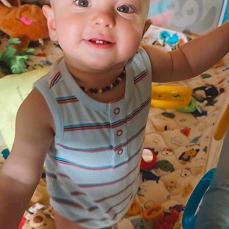 Trevor is registered to the contest to win money with this photo: arm, baby, blanket, child, colorful, curious, face, happy, indoor, infant, necklace, play_area, playpen, portrait, smiling, soft_toys, striped_shirt, stuffed_animals, toddler, toys