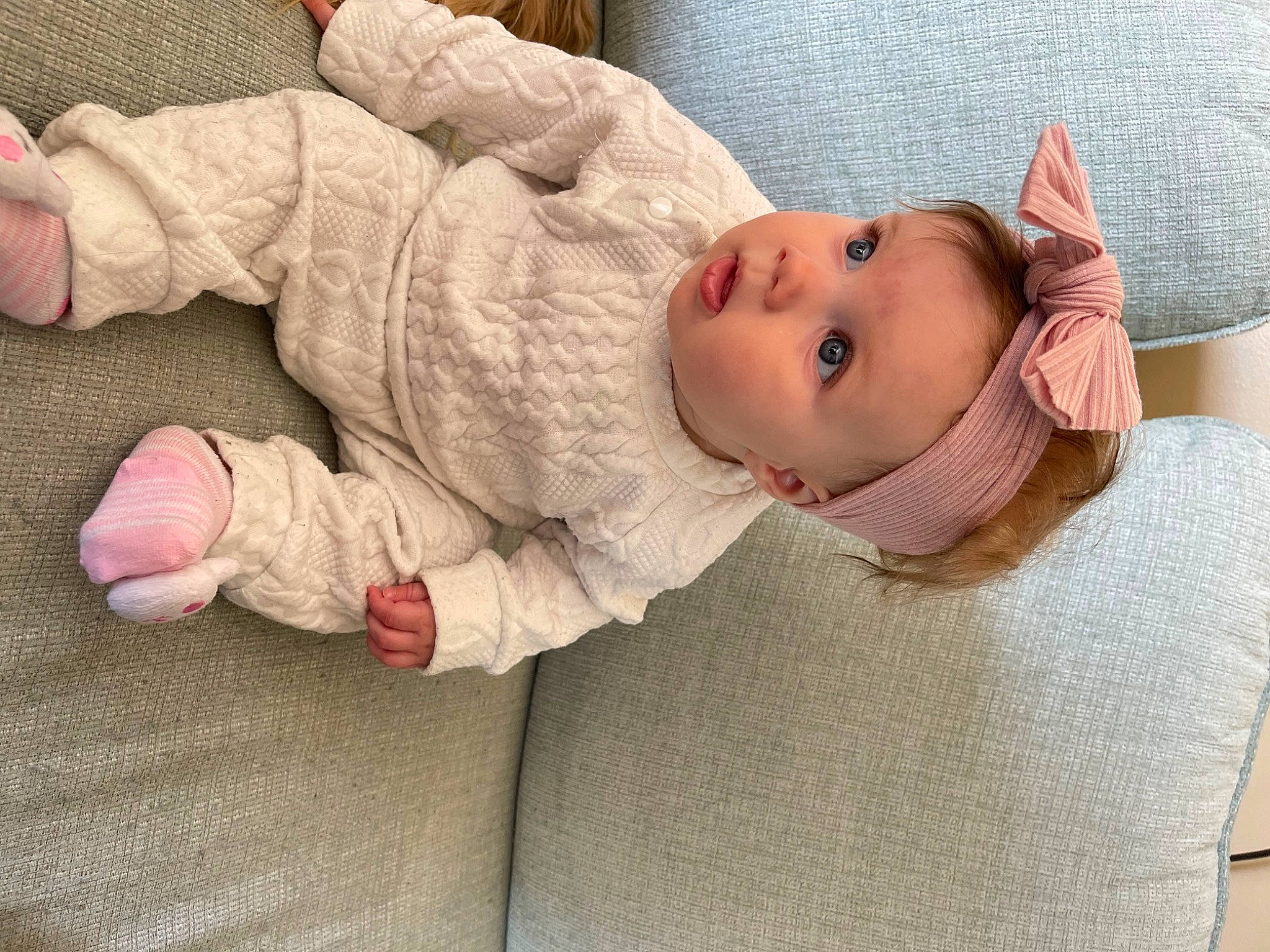 Kailani is registered to the contest to win money with this photo: baby, baby_toddler_clothing, cheek, child, comfort, eye, floor, flooring, hand, hat, headgear, human_body, linens, lip, nose, person, sitting, skin, sleeve, surprise