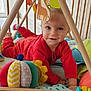 baby, child, toy, giraffe, playmat, wooden_structure, colorful, red_clothing, smiling, indoor, cushion, pillow, face, hand, foot, soft_toys, pattern, fabric, floor, window