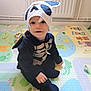 baby, child, clothing, costume, cute, face, floor, hat, headwear, indoor, infant, play_mat, playtime, portrait, sitting, skeleton, smile, toddler, toy, young_child