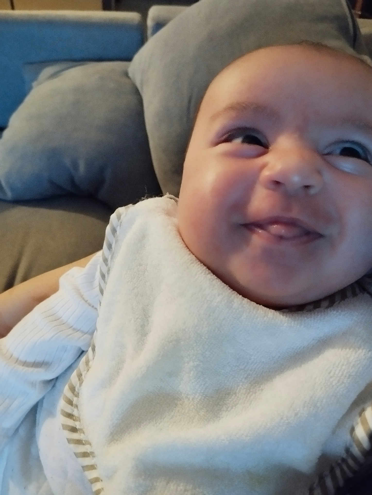 Nahila a rejoint le concours — aidez-le/la à gagner de superbes lots ! baby, close_up, smile, tongue_out, bib, striped_clothing, couch, pillows, indoor, face, infant, child, happy, cozy, soft_furniture, cute, young_child, portrait, relaxing, home