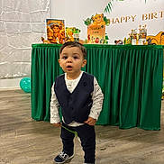 Nahïl participe au concours pour gagner de l'argent avec cette photo : balloon, birthday_party, celebration, child, curious_expression, decorations, floor, green_tablecloth, indoor, lion_king, pants, party, person, shoes, smiling, table, toddler, vest, wooden_floor, young_child