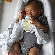 Issac participe au concours pour gagner de l'argent avec cette photo : baby, infant, bottle, feeding, sleeping, blanket, striped_clothing, onesie, cushion, white, soft, peaceful, indoors, child, resting, hand, foot, face, head, comfort