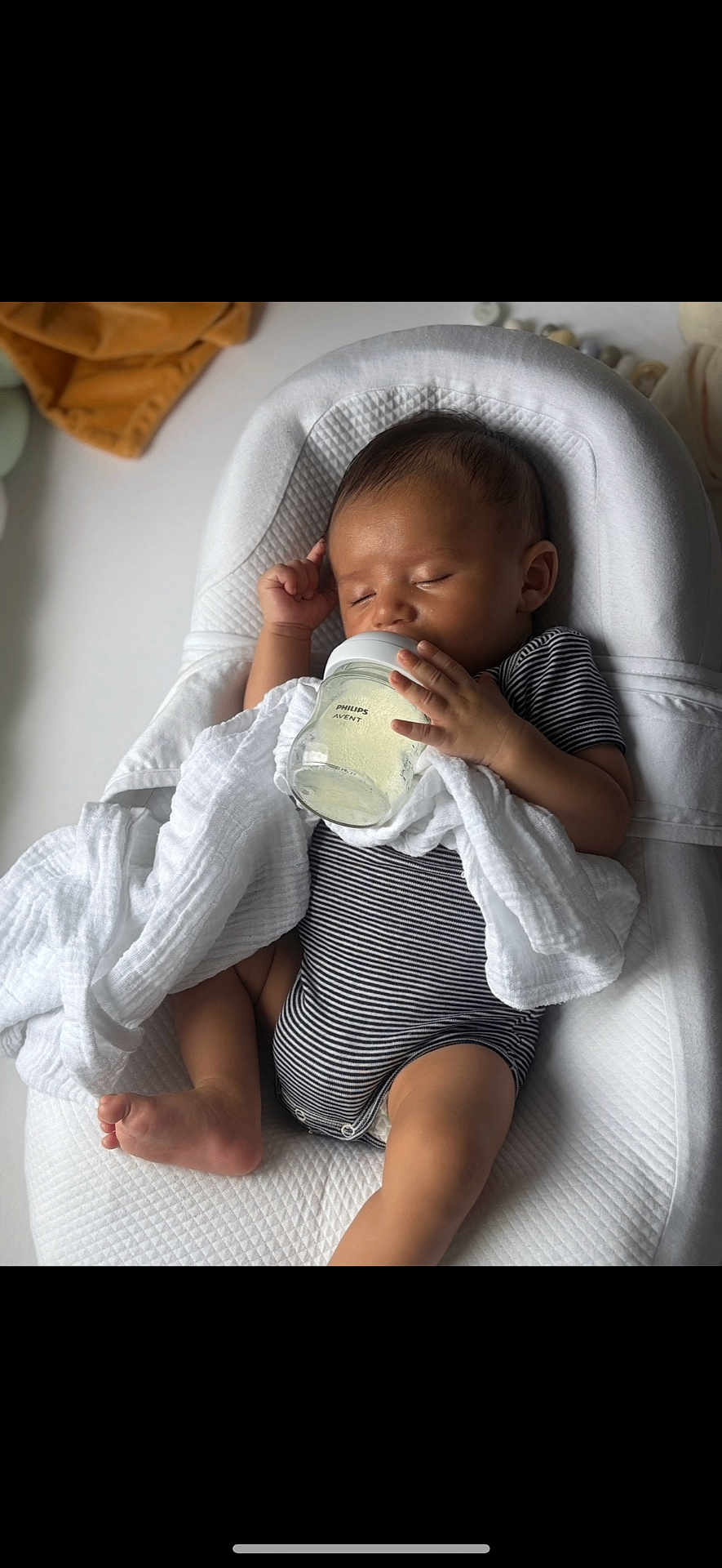 Issac participe au concours pour gagner de l'argent avec cette photo : baby, infant, bottle, feeding, sleeping, blanket, striped_clothing, onesie, cushion, white, soft, peaceful, indoors, child, resting, hand, foot, face, head, comfort