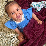Naïla a rejoint le concours — aidez-le/la à gagner de superbes lots ! baby, smiling, blue_dress, blanket, bedspread, patterned, indoors, child, happy, cute, person, infant, face, hair, skin, foot, hand, sitting, cozy, warm