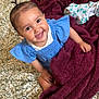 baby, smiling, blue_dress, blanket, bedspread, patterned, indoors, child, happy, cute, person, infant, face, hair, skin, foot, hand, sitting, cozy, warm